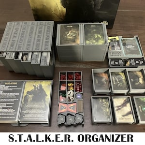 Op de afbeelding: Een grijze en witte organizer voor het bordspel S.T.A.L.K.E.R. De organizer heeft meerdere compartimenten voor het opbergen van de spelonderdelen, waaronder kaarten, tokens en dobbelstenen. De organizer is gelabeld met de titel van het spel en de woorden "Mission" en "Basic Actions".