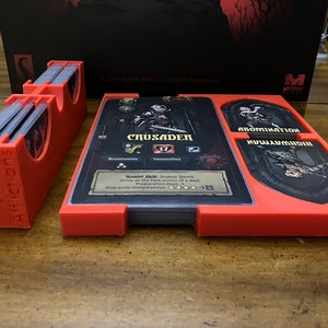 K&ouml;nnte beinhalten: Rote 3D-gedruckte Kartenhalter f&uuml;r ein Brettspiel mit dem Text "Diseases, Virtues, Afflictions". Die Halter befinden sich neben Spielkarten mit den Charakteren "Crusader", "Abomination" und "Highwayman".