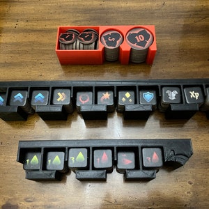 K&ouml;nnte beinhalten: Ein Set aus schwarzen und roten Spielorganisatoren f&uuml;r Brettspiel-Token. Die Organizer umfassen Schlitze f&uuml;r verschiedene Token mit Symbolen und Zahlen sowie einen roten Beh&auml;lter f&uuml;r M&uuml;nzen. Die Token haben Symbole wie Pfeile, Schilde und Erfahrungspunkte.