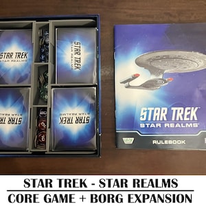 May include: A Star Trek Star Realms board game set. The game box contains card decks, dice, and tokens. A rulebook with a spaceship graphic is also included. The text at the bottom reads: "STAR TREK - STAR REALMS CORE GAME + BORG EXPANSION."