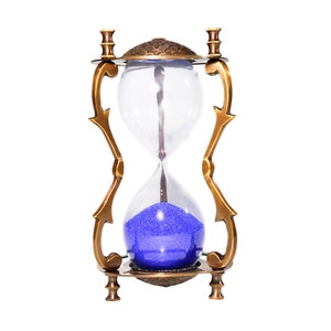 May include: An hourglass with a brass-colored metal frame and clear glass bulbs. The sand inside is a vibrant blue. The frame has decorative, curved supports and a detailed top and bottom. A classic decorative item.