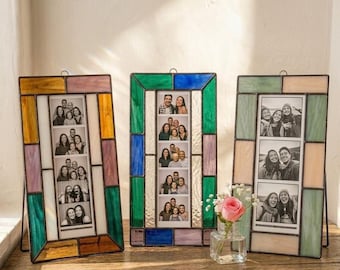 Könnte beinhalten: Drei Glasmalerei-Fotorahmen mit Familienfotos. Die Rahmen haben ein rechteckiges Design mit farbigen Glaspaneelen in Grün-, Blau-, Lila-, Gelb- und Beigetönen. Jeder Rahmen fasst mehrere Fotos.