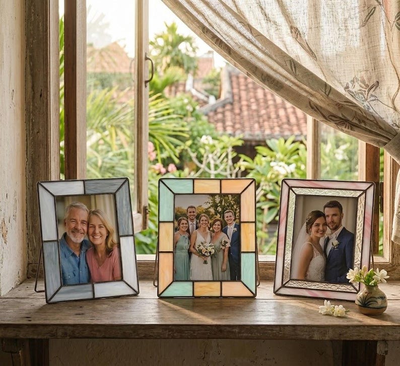 K&ouml;nnte beinhalten: Drei dekorative Fotorahmen mit R&auml;ndern im Glasmalerei-Stil. Die Rahmen sind in Blau-, Pastellgelb- und Rosat&ouml;nen gehalten und halten jeweils ein Foto. Die Rahmen werden auf einer Holzoberfl&auml;che in der N&auml;he eines Fensters ausgestellt.
