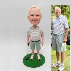 May include: A custom bobblehead figurine of a person wearing a light green and white striped shirt, light green shorts, and white shoes. The figurine holds a golf club and stands on a green base.  A photograph of the same person in similar attire is shown next to the figurine.