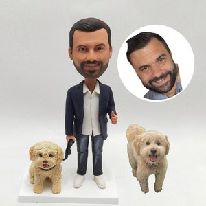 May include: A custom bobblehead figurine of a person wearing a blue blazer, white shirt, and blue jeans. The figurine is holding a lead attached to a small, light brown dog. The figurine is standing on a white base. A close-up of the person's face is shown in a circle.