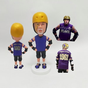 May include: A custom bobblehead figure of a roller derby player wearing a yellow helmet, purple jersey with the text "Papa Crisis 1961", black shorts, and knee pads. The figure is standing on a white base.