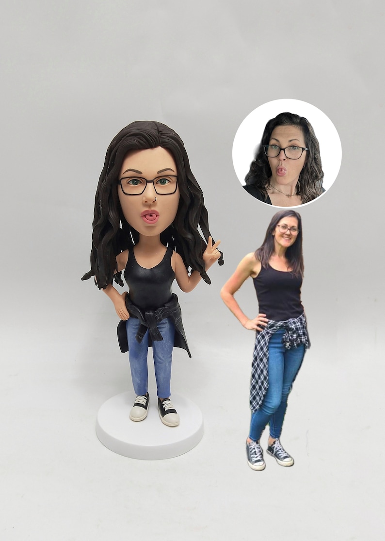 May include: Customizable bobblehead figurine of a person wearing glasses, a black tank top, blue jeans, and sneakers. The figurine has dark brown wavy hair and is shown making a peace sign.  A smaller image shows the same person with a similar expression. The figurine is on a white base.