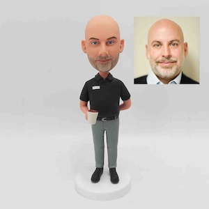 May include: A custom bobblehead figurine of a person wearing a black polo shirt and gray pants. The figurine is holding a coffee cup. The figurine is shown next to a photograph of the same person. The bobblehead is a personalized gift, perfect for corporate events, birthdays, or other special occasions.  The figurine is made of high-quality materials and is designed to last. The custom bobblehead is a unique and memorable gift that is sure to be treasured for years to come.