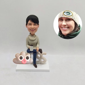 May include: A custom bobblehead figurine of a person sitting on a white base with the word "BOSS". The figurine is holding a coffee mug. A small cloud with eyes and a pink mouth is on the base. A photo of the person is in the background.