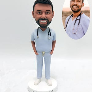 Könnte beinhalten: Eine personalisierte Bobblehead-Figur eines Arztes, der eine hellblaue OP-Jacke und eine Hose trägt. Die Figur hat ein Stethoskop um den Hals und steht auf einem weißen Sockel mit dem Namen "Deepak P. Maharaj, DO" darauf.
