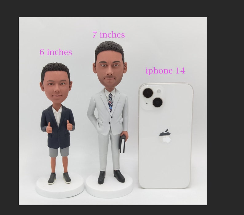 May include: Two custom bobbleheads, one 6 inches and one 7 inches tall, stand next to an iPhone 14.  Both bobbleheads wear suits; one is navy blue, the other light gray.  They are displayed on small white bases.  The height of each bobblehead is indicated in inches.