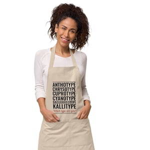 May include: A beige apron with black text that reads "ANTHOTYPE, CHRYSOOTYPE, CUPROTYPE, CYANOTYPE, DAGUERREOTYPE, KALLITYPE" and "Which type are you?" in red text.