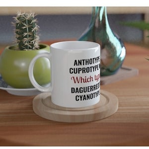 May include: White ceramic mug with black text that reads "ANTHOTYPE, CUPROTYPE, Which type, DAGUERREOTYPE, CYANOTYPE". The word "type" is in red.