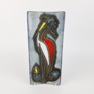 May include: A rectangular ceramic wall plaque with a stylized design of two birds in shades of red, white, blue, and yellow on a gray background.
