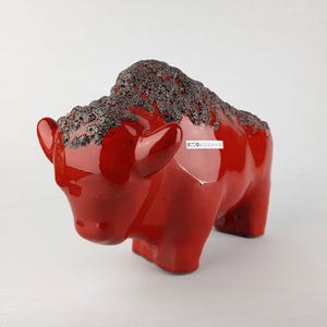 Könnte beinhalten: Rote Keramik-Bison-Skulptur mit einem gesprenkelten grauen Überzug auf der Rückseite. Die Skulptur ist seitlich mit "Otto Keramik" signiert.
