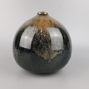 May include: A round, dark green ceramic vase with a glossy finish. The vase has a speckled brown glaze that creates a unique pattern.