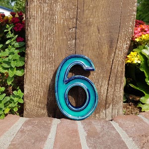 May include: A ceramic house number six featuring a glossy finish with a gradient of deep navy blue at the edges transitioning into a vibrant turquoise center. The number has a rounded, bold typeface and a smooth, reflective surface texture.