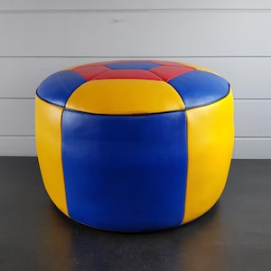 May include: A round, blue, yellow and red ottoman with a geometric pattern. The ottoman is made of leather and has a black trim.