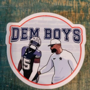 May include: A circular sticker featuring the text "DEM BOYS" in blue and white, with a red border. The sticker depicts two figures: a football player in a navy and silver uniform and a coach in a white shirt and cap.