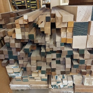 May include: A large stack of various wood pieces, including square and rectangular blocks, in different shades of brown and beige. Some of the wood pieces have a green stain on the ends.