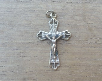 Peut inclure: Pendentif crucifix argenté avec une représentation détaillée de Jésus-Christ. La croix a des bords décoratifs et une petite boucle pour une chaîne. Le pendentif est présenté sur une surface en bois brun clair.