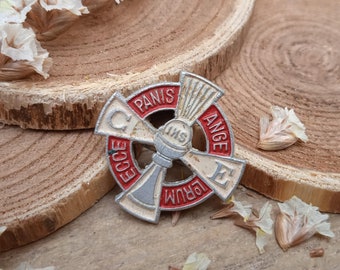 Peut inclure: Une épingle en métal blanc avec des accents rouges. L'épingle représente une croix avec les mots "ECCE PANIS" et "ANGE LUPUM" sur les bords. Le centre de la croix présente une image stylisée d'un calice avec les lettres "IHS" au-dessus.