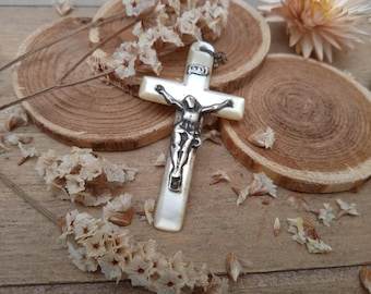 Peut inclure: Un crucifix en nacre blanche avec une figurine de Jésus en argent. Le crucifix est posé sur une surface en bois avec des fleurs séchées.