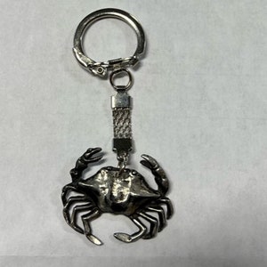 May include: Silver keychain featuring a detailed crab design. The keychain has a silver chain and a silver ring.