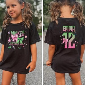 May include: Black t-shirt with a pink and green graphic design featuring a witch's hat, a bow, and the text "Wicked Birthday Girl". The back of the shirt has a pink and green graphic design featuring a witch's hat, a bow, and the text "Emma 12".
