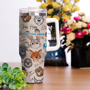 Puede incluir: Un vaso de acero inoxidable con ilustraciones de personajes de dibujos animados y el texto "Judy Hopps" y "Custom Name". El vaso tiene un asa y tapa blancas, con un fondo beige.
