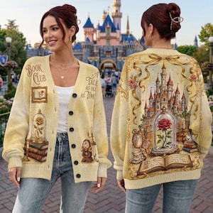 Puede incluir: Un cárdigan de color crema con botones y un diseño estampado de un castillo, una rosa en una cúpula de cristal, libros y un personaje de reloj. El texto "Book Club" y "A Tale As Old As Time" está impreso en el frente, con un castillo en la espalda.