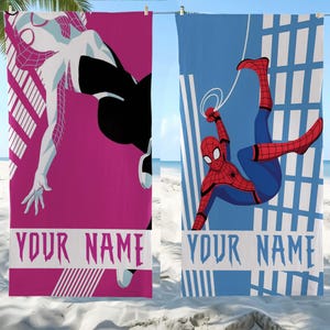 May include: Two beach towels with superhero designs. One is pink with a white and black Spider-Gwen illustration and the text "YOUR NAME". The other is blue with a Spider-Man illustration and the text "YOUR NAME".