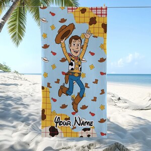 Puede incluir: Una toalla de playa azul claro con un personaje de dibujos animados de vaquero sosteniendo un sombrero, con el texto "Your Name" en la parte inferior. La toalla tiene un patr&oacute;n repetido de sombreros de vaquero, botas y insignias de sheriff.