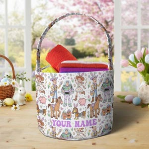 May include: A white Easter basket with a handle, featuring a colorful cartoon design of characters. The basket is filled with folded towels. The text "YOUR NAME" is printed on the front of the basket.