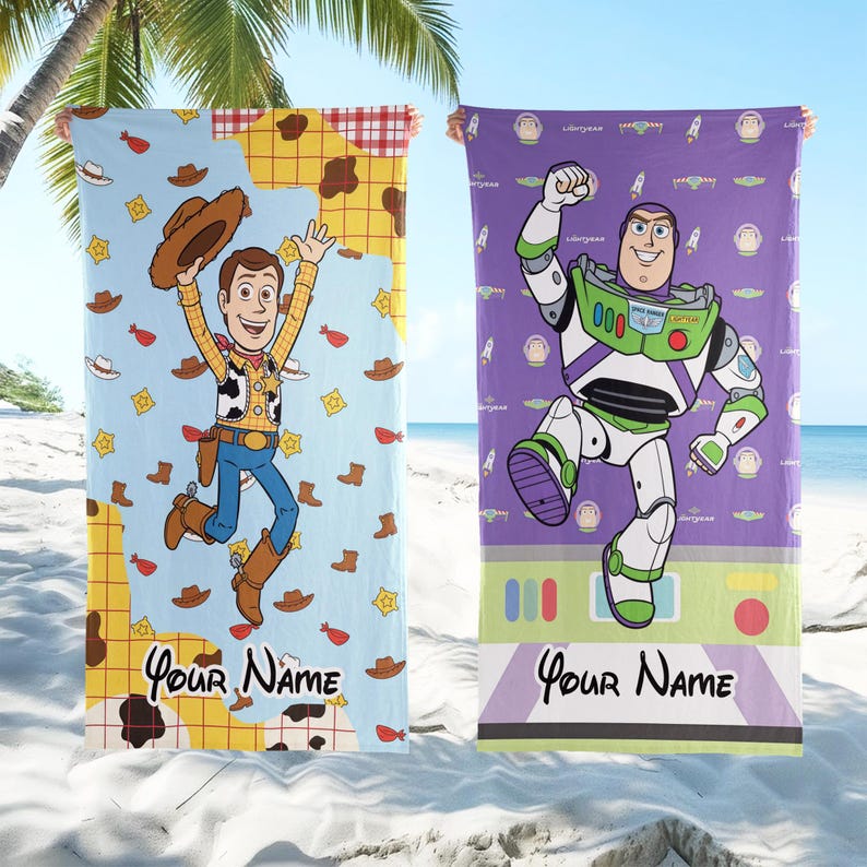 Puede incluir: Dos toallas de playa con personajes de Toy Story. Una toalla tiene un fondo azul claro con Woody, la otra tiene un fondo morado con Buzz Lightyear. Ambas toallas tienen el texto "Your Name" en la parte inferior.
