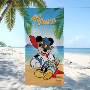 以下が含まれることがあります： サングラスと帽子をかけたミッキーマウスがビーチボールとバケツを持っているビーチタオル。背景にはビーチのシーンがあり、「Name」という文字が筆記体で書かれています。