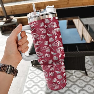 Puede incluir: Un vaso grande y aislado con asa y tapa blancas. El vaso est&aacute; cubierto con un estampado de coches de carreras blancos, banderas a cuadros y rayos sobre un fondo granate. Incluye una pajita blanca.