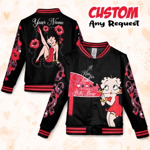 May include: Black bomber jacket featuring Betty Boop illustrations and the text "A Kiss for Luck Betty Boop" and "Your Name". The jacket has red and white accents, including striped cuffs and collar, and decorative floral patterns.