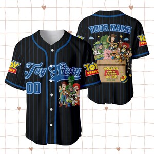 May include: A black baseball jersey with blue pinstripes, featuring Toy Story characters on the front and back. The front displays the Toy Story logo and the number 00. The back shows characters in a box with the text YOU'VE GOT A FRIEND IN ME.