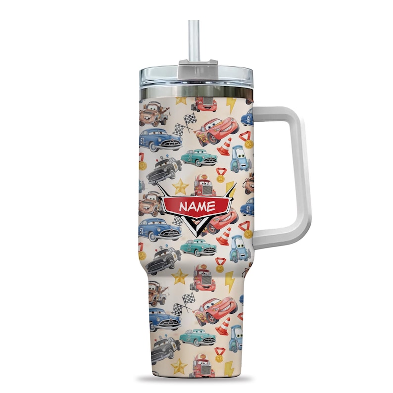 May include: A tall, insulated tumbler with a white handle and a straw. The tumbler features a repeating pattern of cartoon cars, race flags, and stars on a beige background. A red banner with the word "NAME" is centered on the tumbler.