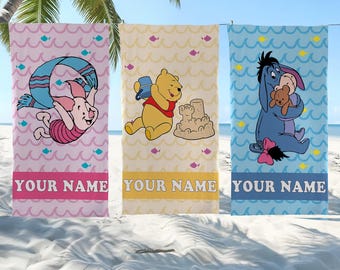 Puede incluir: Tres toallas de playa rectangulares con personajes de Winnie the Pooh. La toalla rosa muestra a Piglet, la amarilla a Winnie the Pooh con un castillo de arena y la azul a Igor. Cada toalla tiene un patrón de ondas y un recuadro con el texto YOUR NAME.