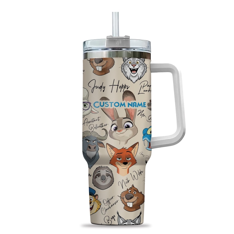 Puede incluir: Un vaso beige con caras de personajes de dibujos animados de Zootopia, incluyendo a Judy Hopps y Nick Wilde. El vaso tiene un asa blanca, una tapa plateada y una pajita. El texto "CUSTOM NAME" tambi&eacute;n es visible.