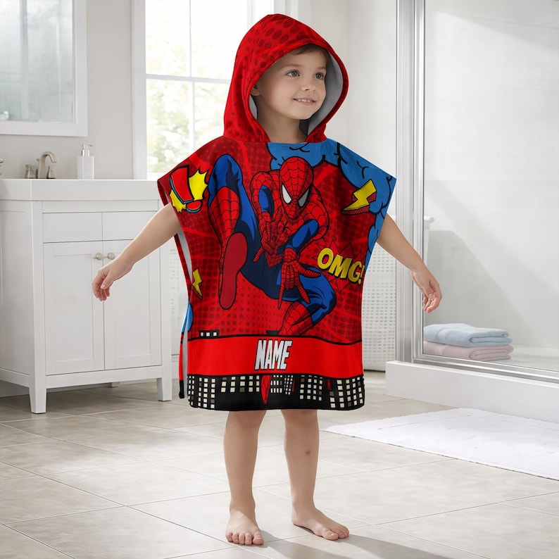 May include: Red hooded beach towel featuring a Spider-Man graphic. The towel has a red and black cityscape design at the bottom, with the word "NAME" printed on a red banner. The hood is red with a dotted pattern.