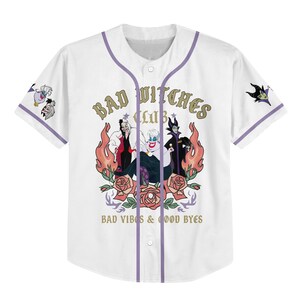 Puede incluir: Camiseta de b&eacute;isbol blanca con ribetes morados y las palabras "Bad Witches Club" en letras doradas. La camiseta presenta un gr&aacute;fico de tres villanos de dibujos animados rodeados de llamas y rosas. La frase "Bad Vibes & Good Byes" est&aacute; impresa debajo.
