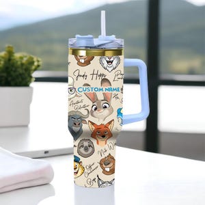 Puede incluir: Un vaso t&eacute;rmico beige con personajes de dibujos animados de Zootopia, con un asa y tapa azul claro. El vaso tiene una pajita y detalles dorados. El texto "CUSTOM NAME" es visible.