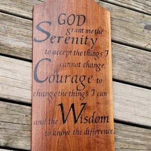 May include: A brown wooden sign shaped like a cutting board with a hole at the top. The text reads: GOD grant me the Serenity to accept the things I cannot change. Courage to change the things I can and the Wisdom to know the difference.