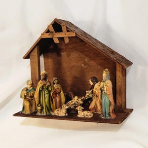 May include: A wooden nativity scene with a brown wooden stable and figurines. The figurines include the three wise men, Mary, Joseph, baby Jesus, and several sheep. The figurines are painted with various colors.