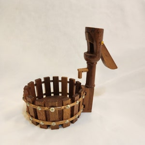 May include: A wooden well with a bucket and a hand crank. The well is decorated with metal accents.