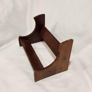 May include: A dark brown wooden display stand featuring two side panels with curved top edges, connected by two horizontal support bars. The structure is assembled with visible metal screws on the exterior of the side panels, creating a sturdy frame.