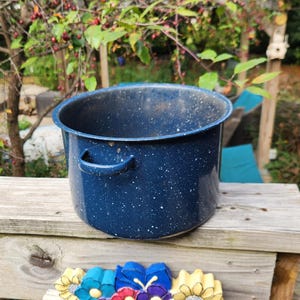 May include: A deep, cylindrical cooking pot with a dark blue enamel finish and a white speckled pattern. The pot features two small, curved side handles and a wide, open top, showcasing a dark interior surface consistent with the exterior finish.